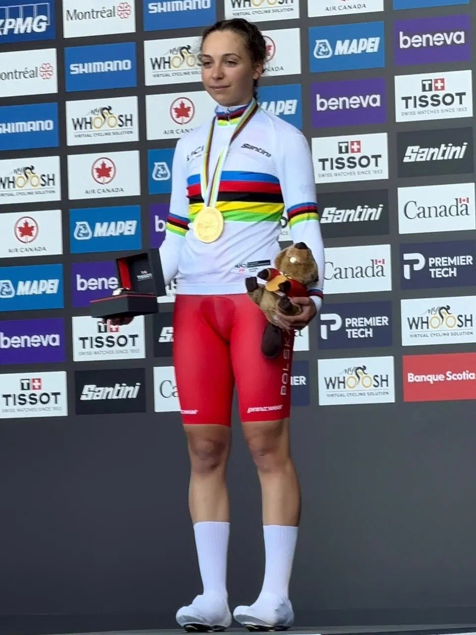 Kolarka w tęczowej koszulce prezentuje medal i trofeum