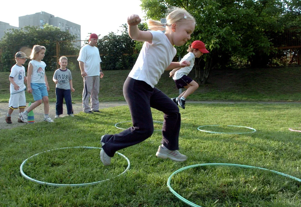 Dziewczynka ćwiczy rzut, a inne dzieci czekają na trawie