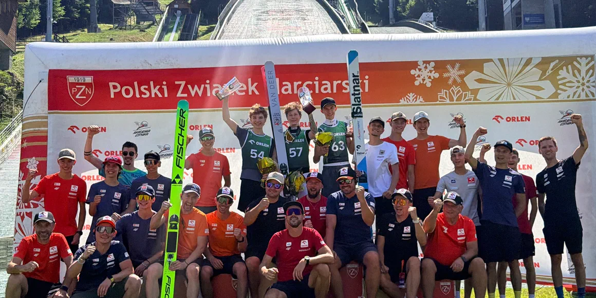 Grupa zawodników i trenerów z nartami przed skocznią